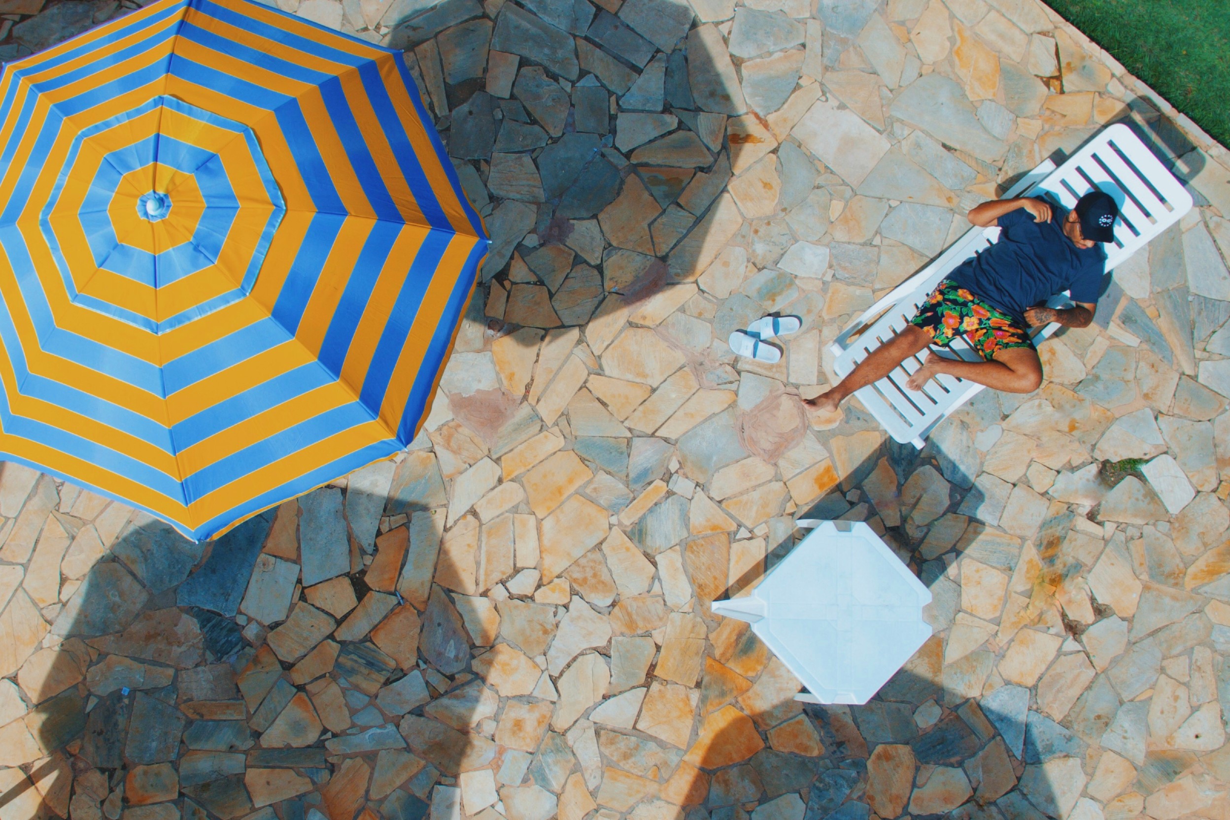 Gestreifter Sonnenschirm auf einer Steinterrasse zusammen mit einem Mann beim Sonnenbaden