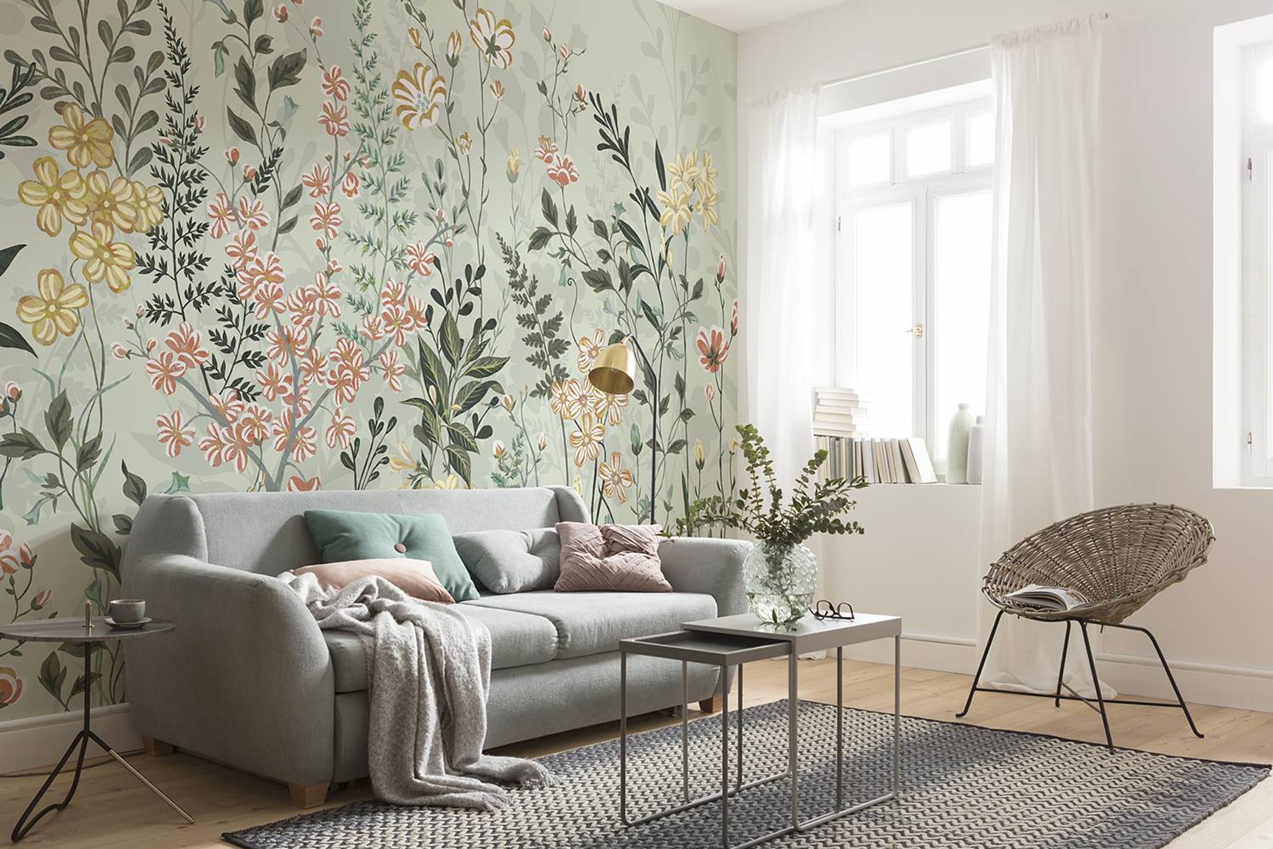 Wand mit bunter Blättertapete, grauem Sofa und feinen Beistellmöbeln.