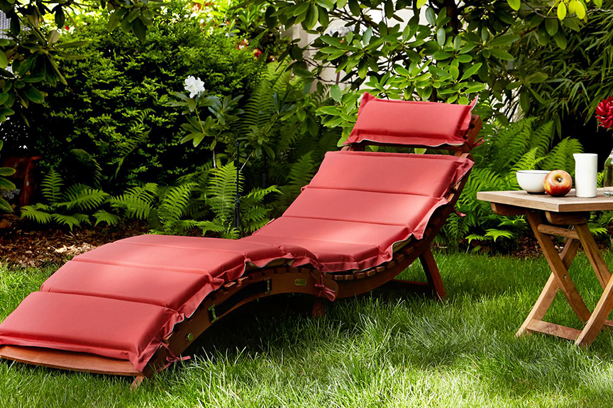Houten ligstoel met rode bekleding in het midden van een groene tuin