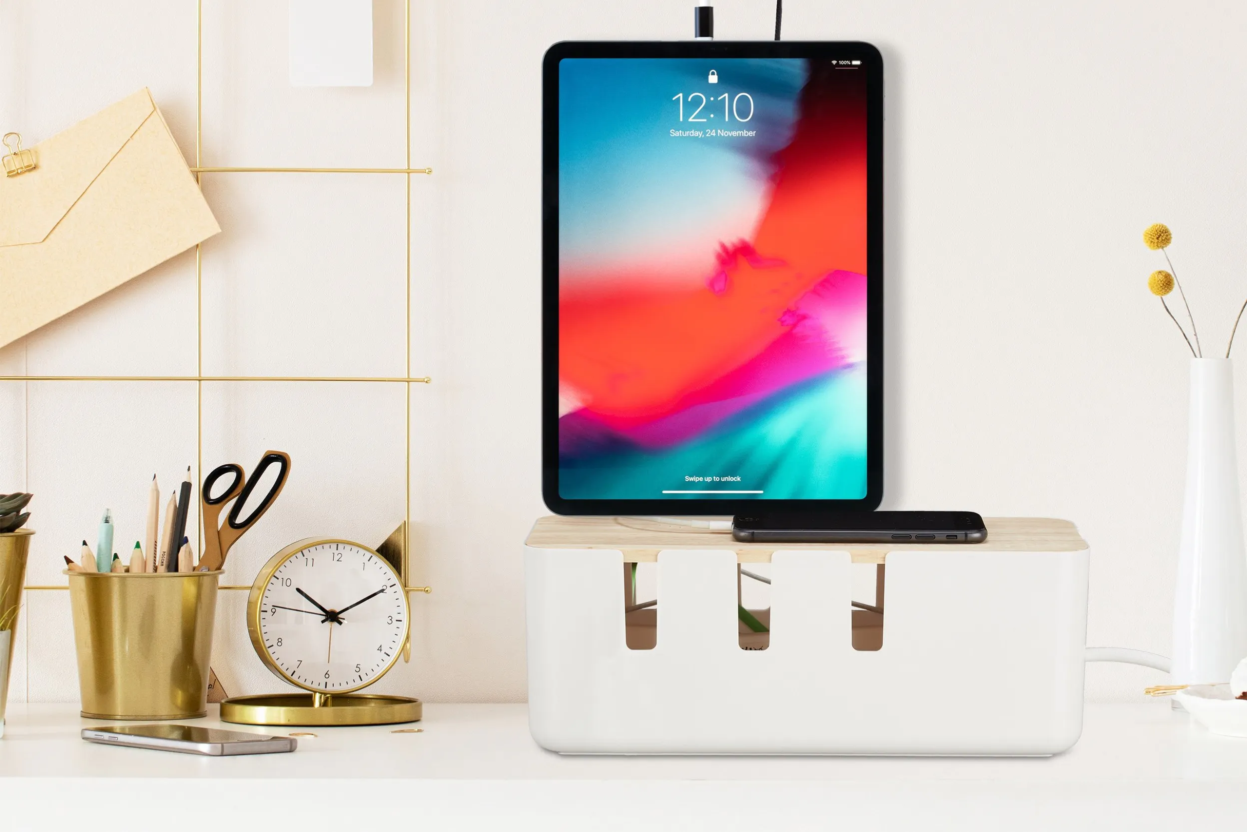 Moderne Kabelbox mit darauf stehendem Tablet zusammen mit goldenen Büroaccessoires