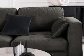 Dunkelgraues Ecksofa Gaillon by Studio Copenhagen im elegant-schlichten Design mit gleichfarbigen Kissen, kombiniert zu einem runden Couchtisch mit weißer Marmor-Tischplatte.