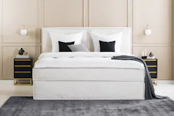 Einrichtungsbeispiel für Hotels: Schlafzimmer mit einem beigen Boxspringbett und Nachttischen in einer eleganten Schwarz-Gold-Kombination, dazu schwarze und weiße Deko und viele Textilien.