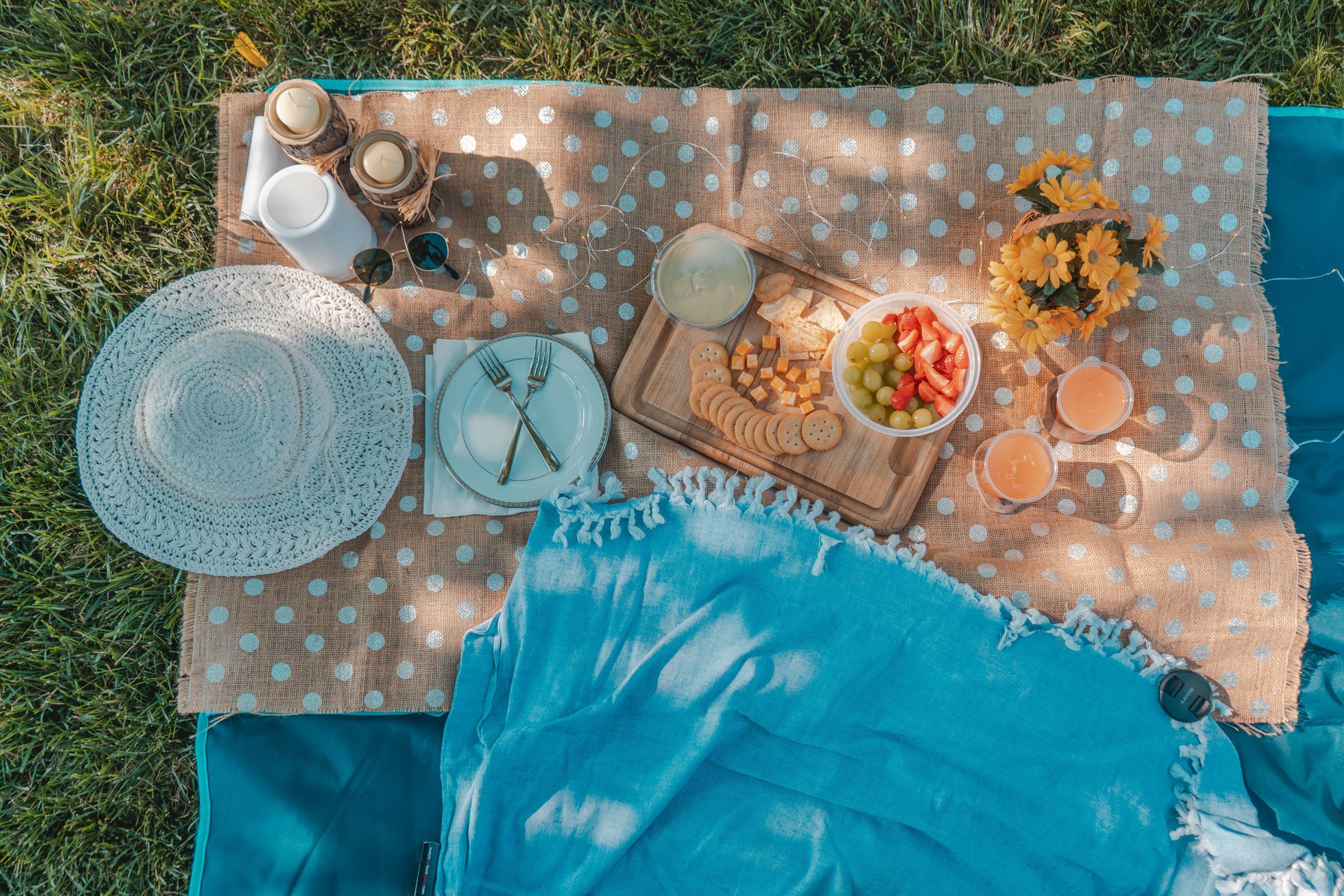 Gepunktete Picknickdecke mit Snacks, Blumen, Sonnenhut und weiteren Accessoires