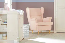 Babyzimmer mit hellen Möbeln sowie rosafarbener Ohrensessel stehend vor gestrichener Wand