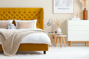 Schlafzimmer im Skandi-Stil vor Samtbett in Senfgelb