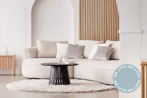 Salon dans des tons neutres : canapé 2 places Buckley de couleur crème et aux formes arrondies, table basse ronde en bois foncé ; canapé Buckley beige dans le salon de @jasmin_laabs, dont le chien dort sur un tapis beige.