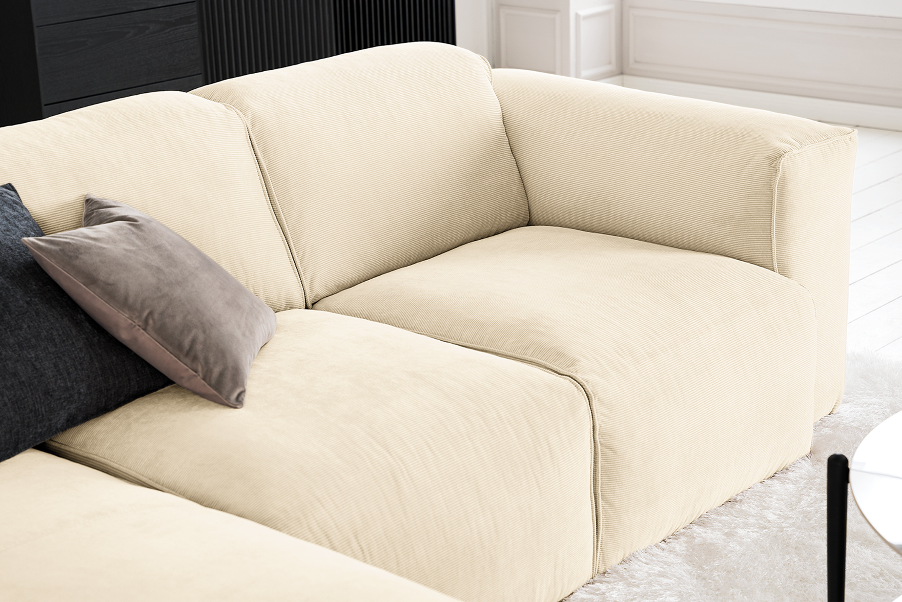 Canapé en velours côtelé blanc cassé Studio Copenhagen, avec un coussin en velours ras gris souris et un coussin en tissu structuré noir.