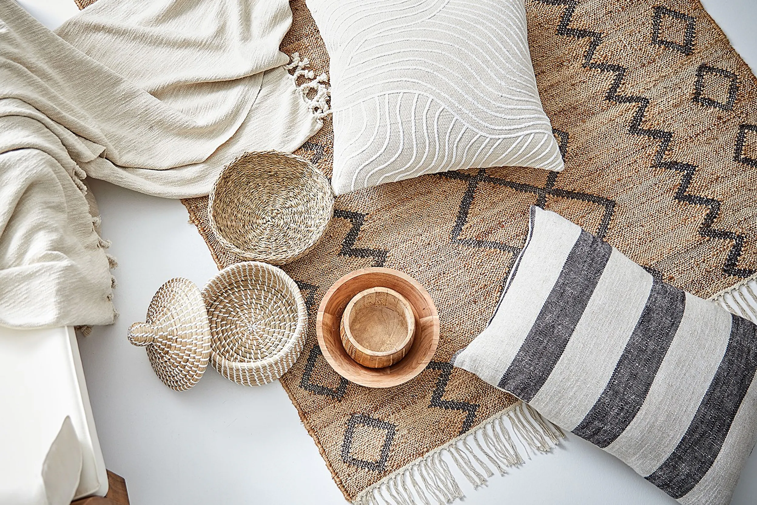 Verschiedene Accessoires aus der Vogelperspektive, darunter Kissen, Teppich, Decke, Körbe und Schalen