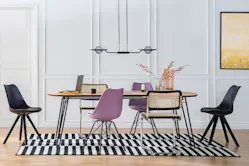 Esszimmer mit Esstisch und Stühlen in Schwarz, Lila und mit Wiener Geflecht auf schwarz-weißem Teppich, dazu eine Pendelleuchte mit Glas sowie ein schwarzes Leiterregal.