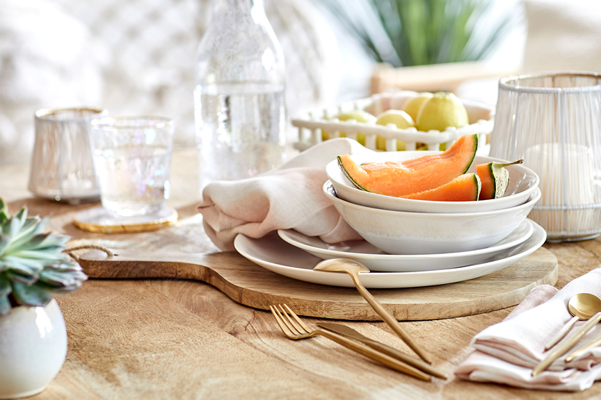 Table de salle à manger en bois avec vaisselle blanche et verres à la bordure dorée, couverts dorés