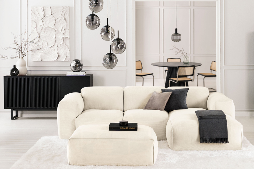 Salon noir et blanc avec canapé blanc Hudson de chez Studio Copenhagen sur un tapis fluffy blanc, avec meubles noirs posés devant des murs blancs et présentant des objets déco noirs et blancs.