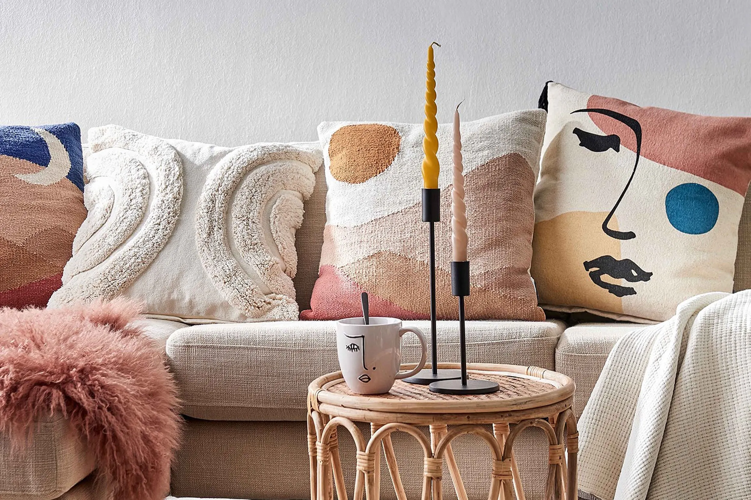 Diverse Kissen in unterschiedlichen Designs hinter einem Tisch mit Tasse und Kerzenständern
