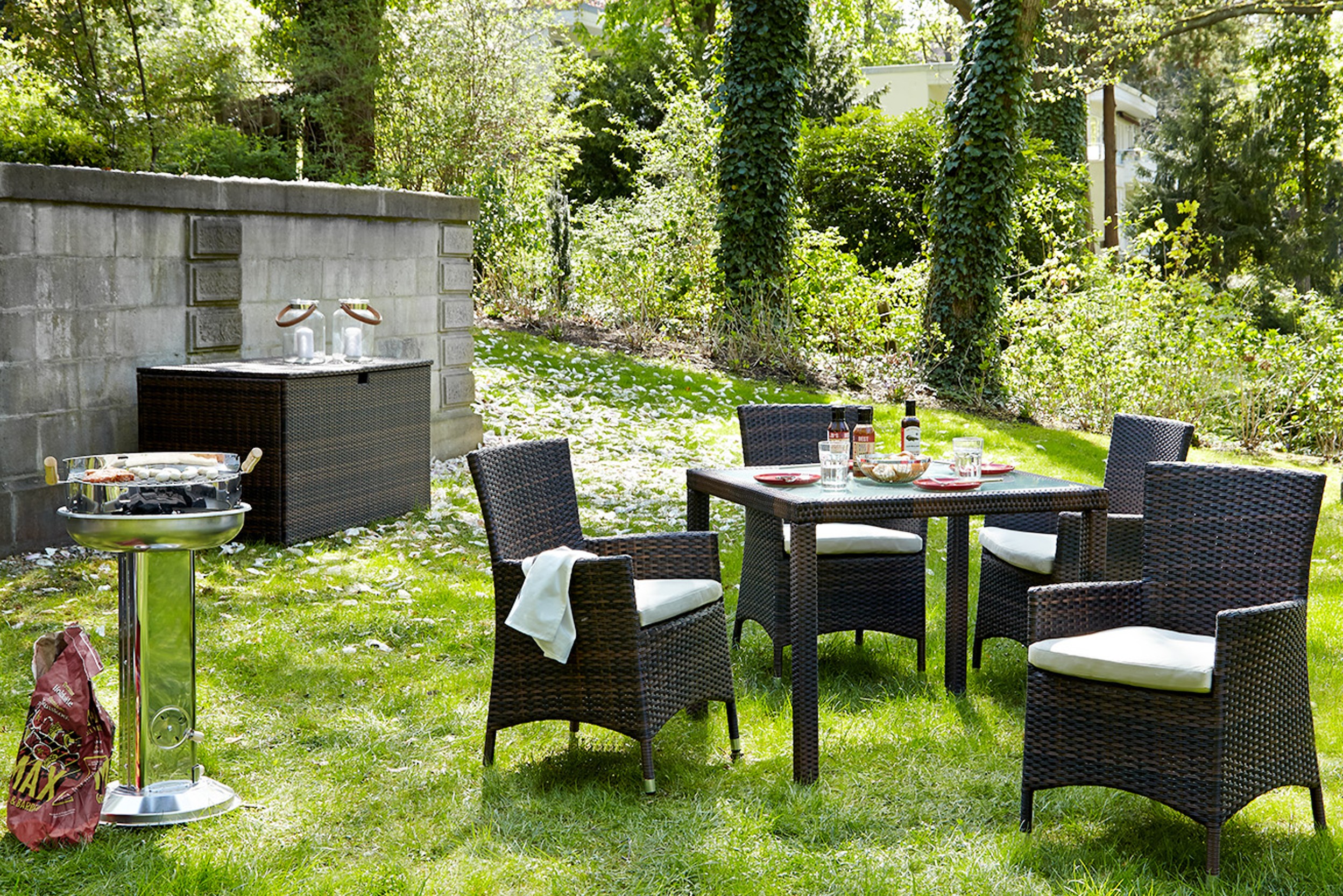 Grüner Garten mit Polyrattan-Essgruppe, Holzkohlegrill und Gartenbox mit Windlichtern