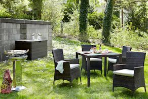 Grüner Garten mit Polyrattan-Essgruppe, Holzkohlegrill und Gartenbox mit Windlichtern