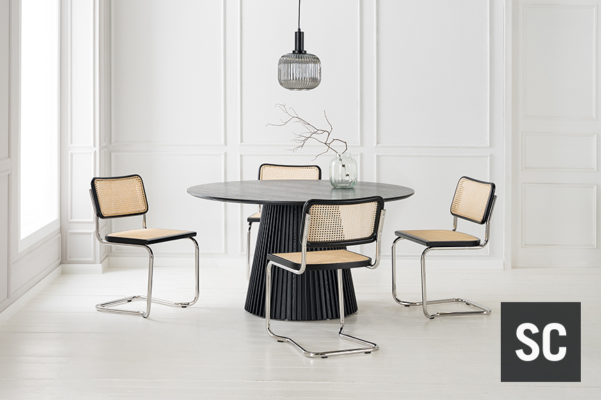 Vier Freischwinger mit Lehnen und Sitzfläche aus Wiener Geflecht, silbernem Stahlrohr und schwarzen Akzenten stehen um einem schwarzen Rundtisch vor weißer Kulisse