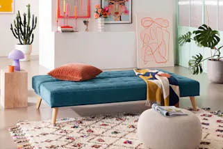 Petrolfarbenes Klappsofa für Übernachtungsgäste, dazu ein Cube-Beistelltisch mit einer lilafarbenen Mushroom-Tischleuchte.