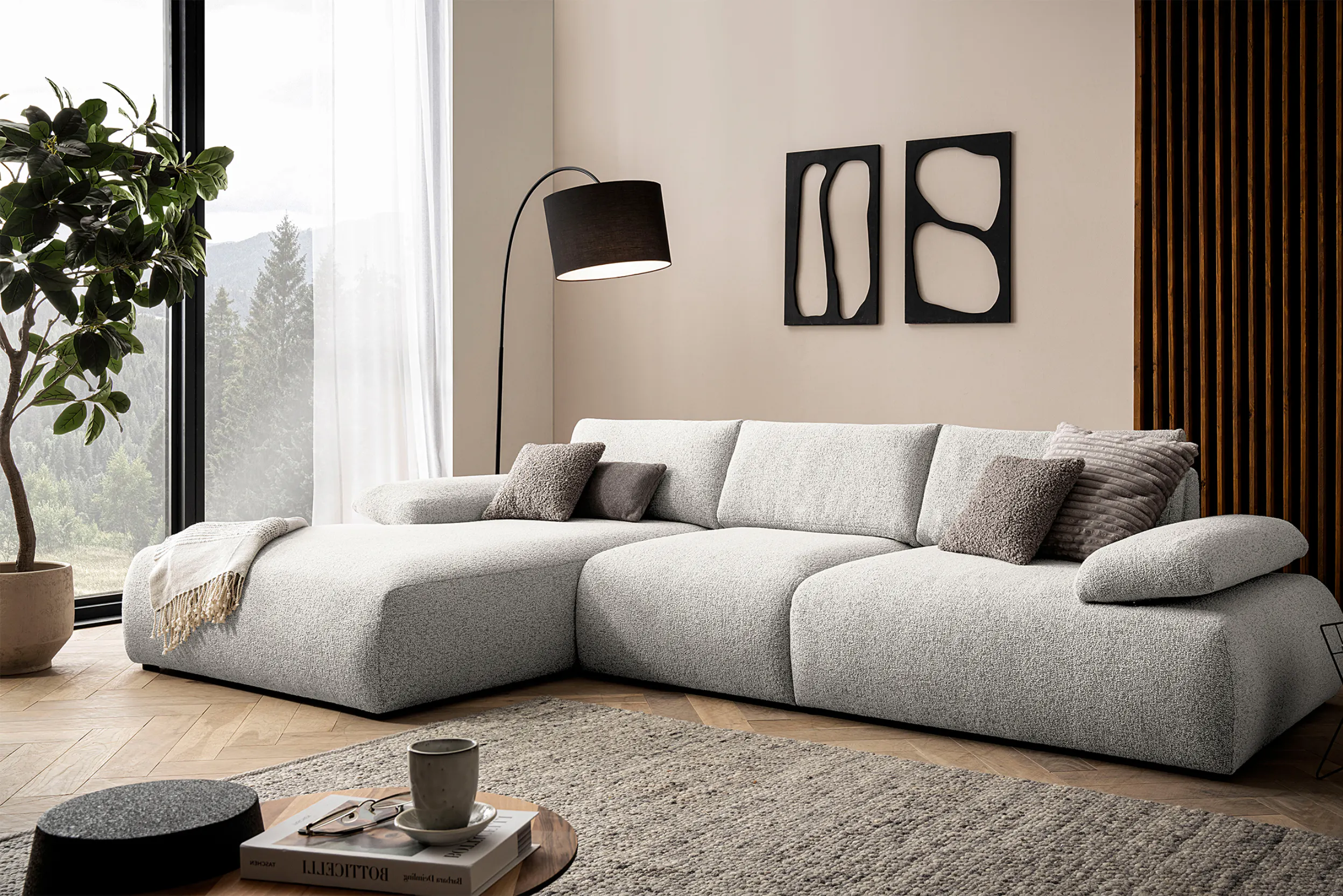 Modernes, niedriges Ecksofa in Hellgrau mit schwarzer Stehlampe und Zimmerbaum.